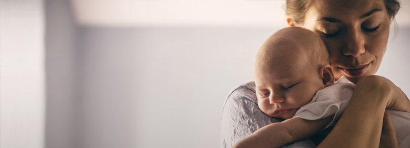 mother holding newborn baby over her shoulder